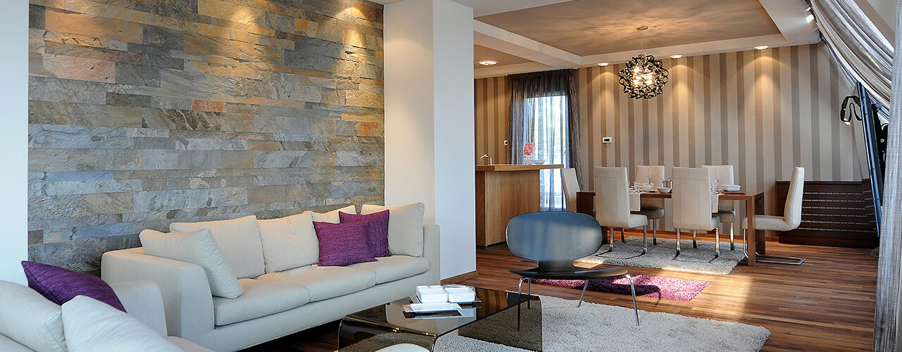 A furnished living room with a stone feature wall and a dining area beyond